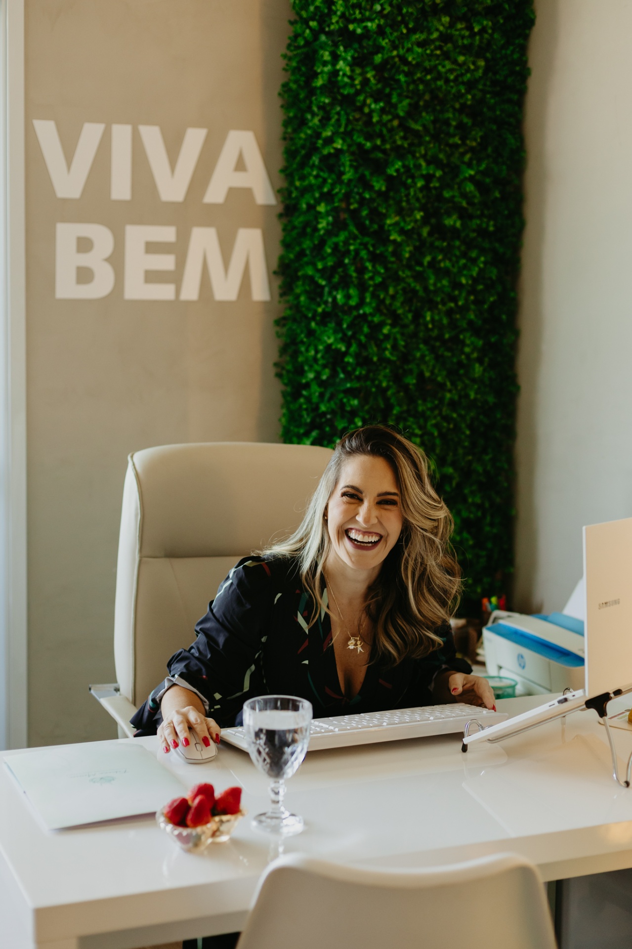 Fabiana Moreira sorrindo no consultório com parede verde ao fundo